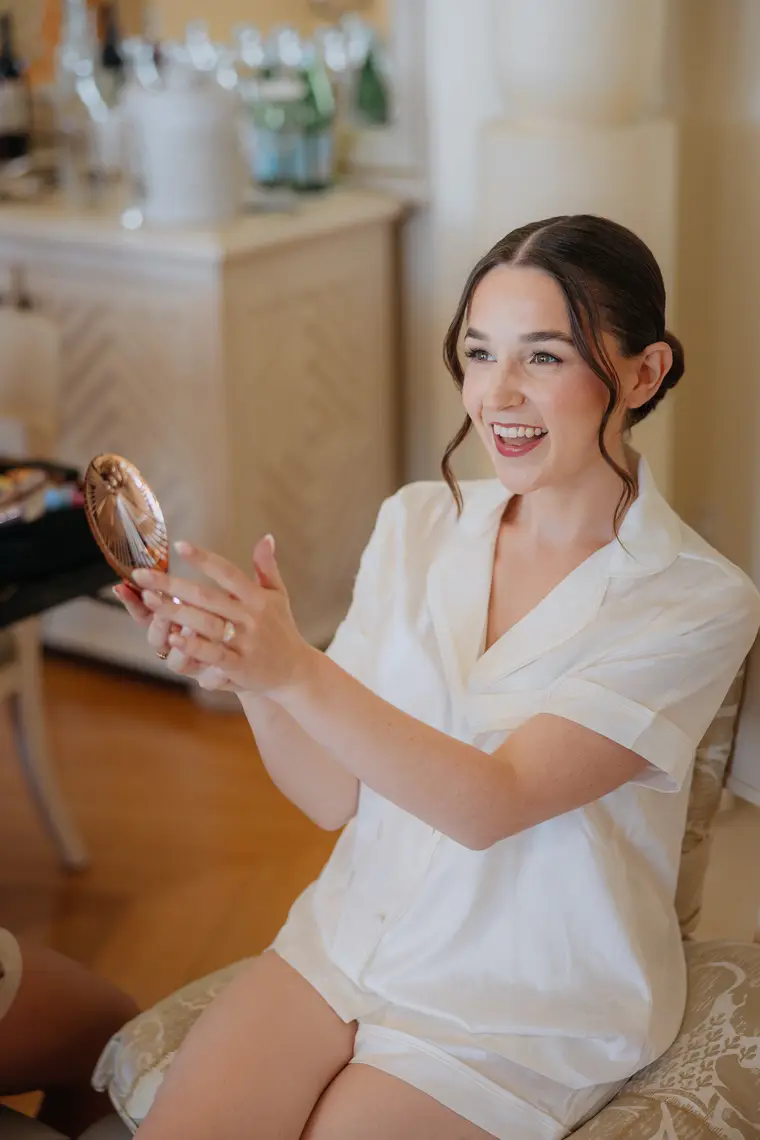Poppy smiling into a hand mirror in her white pyjamas while getting ready