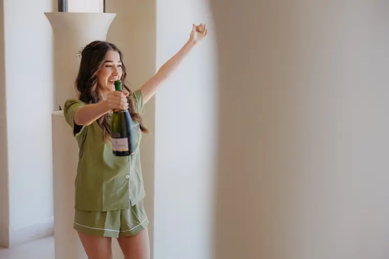 Poppy in green pyjamas celebrating with a bottle of champagne, arm raised