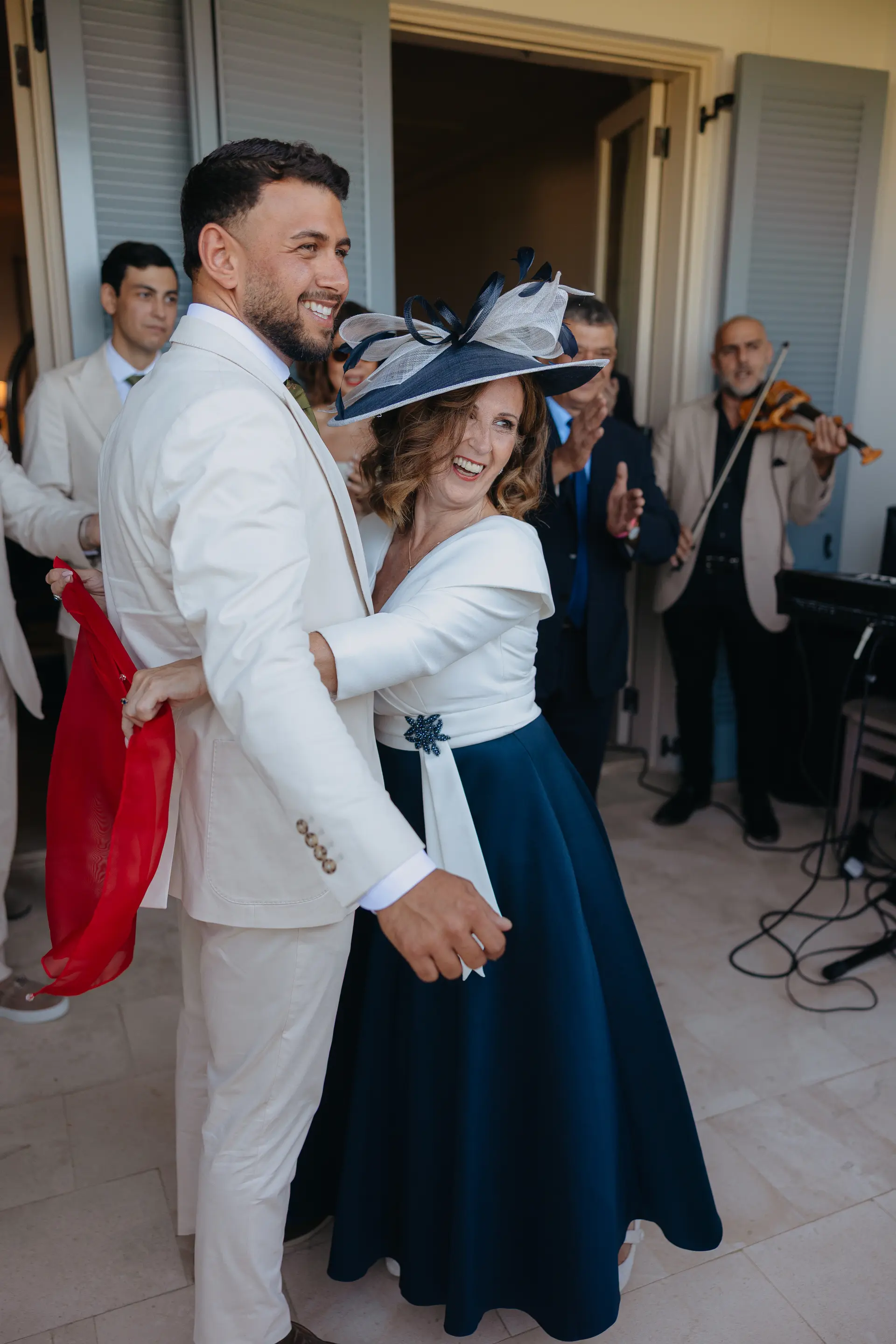 Andrew laughing arm in arm with a woman in a navy hat, red ribbon in hand