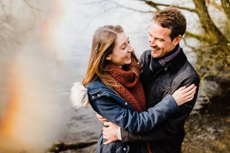 Jana and Alex laughing in a hug beside the water