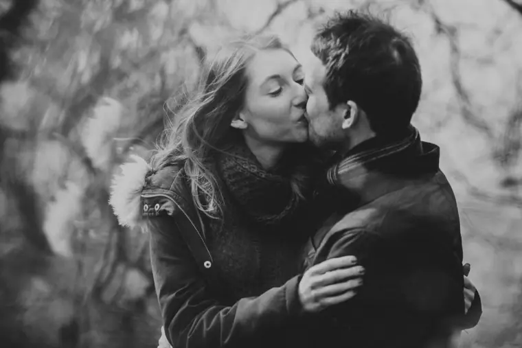 Black-and-white photo of the couple kissing among trees