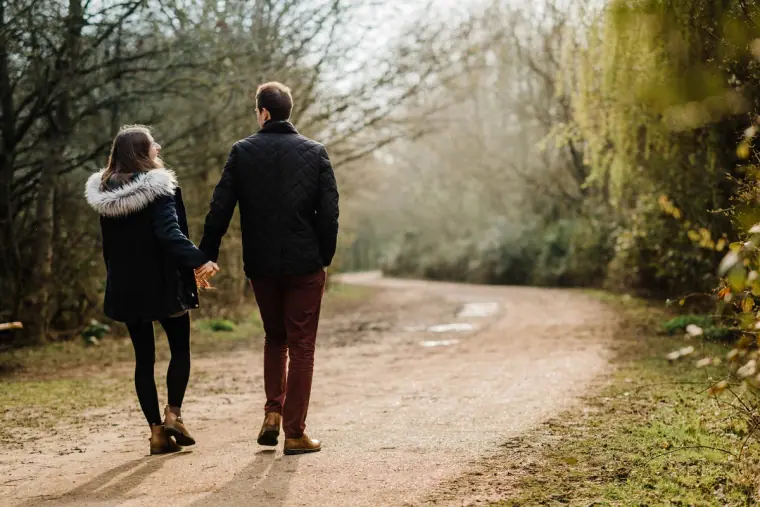 Couple walking hand in hand down a woodland path