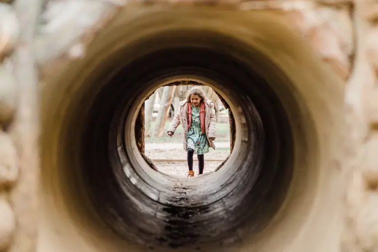 Young girl standing at the far end of a wooden play tunnel