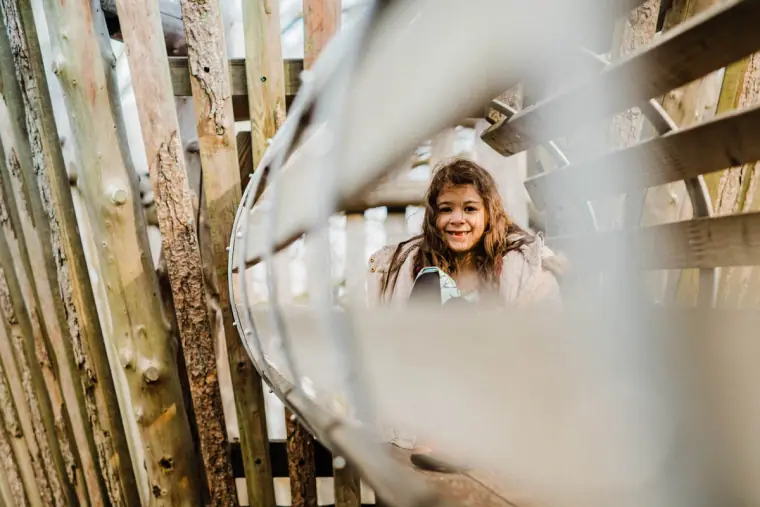 Young girl peeking out from a wooden play structure
