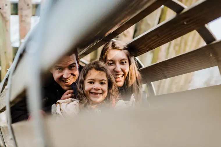 Couple and young girl peering through a wooden climbing frame