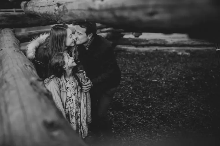 Black-and-white photo of the couple sharing a cuddle with a young girl by a log