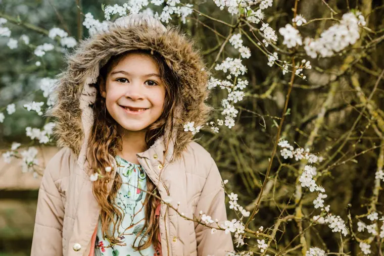 Young girl in a fur-trimmed hood smiling in front of white blossom