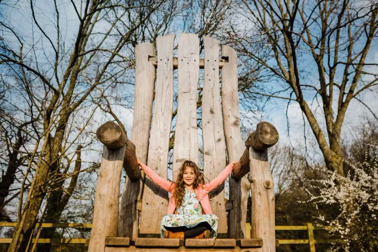 Young girl sitting on a giant wooden throne in a playground