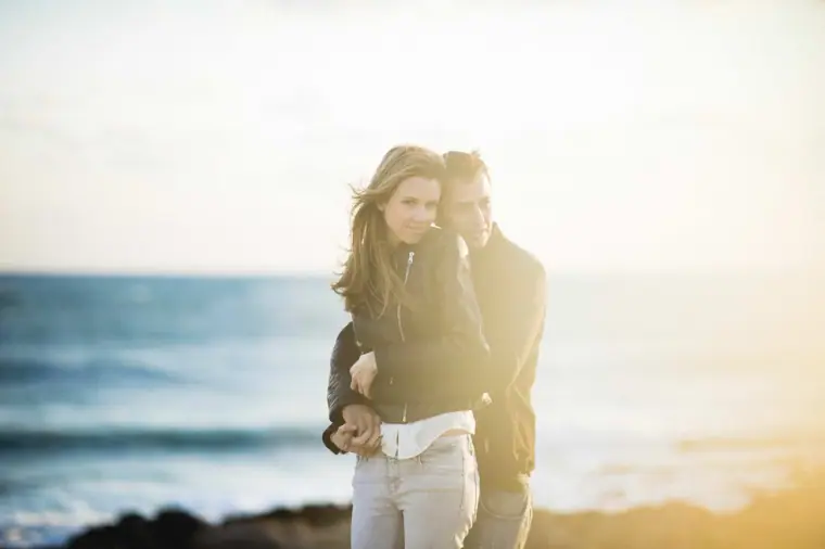 Couple embracing on the shore in hazy backlight, the sea behind them