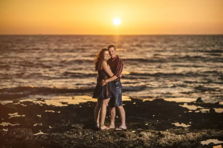 Couple holding each other on the rocks at the water's edge at sunset