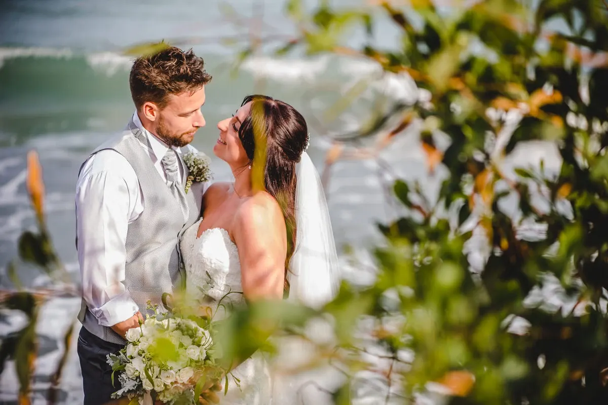 Laura and Lee embracing by the sea, framed by foliage, at Royal Apollonia, Limassol