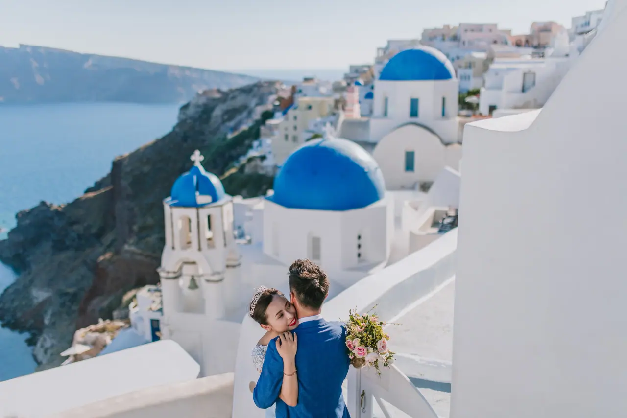 Couple kissing on a white terrace above the blue-domed churches and caldera of Santorini