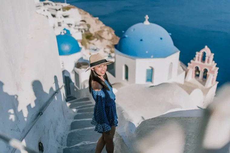 Woman in a blue dress and sun hat on white steps beside a blue-domed church