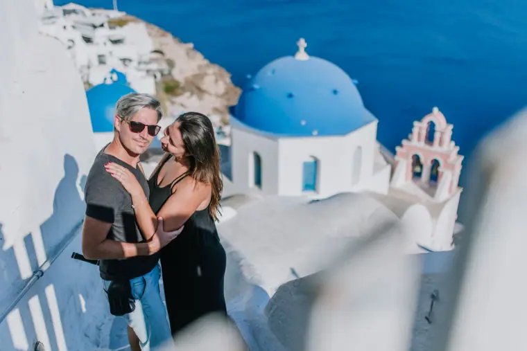 Smiling couple in sunglasses posing by a blue-domed church above the sea