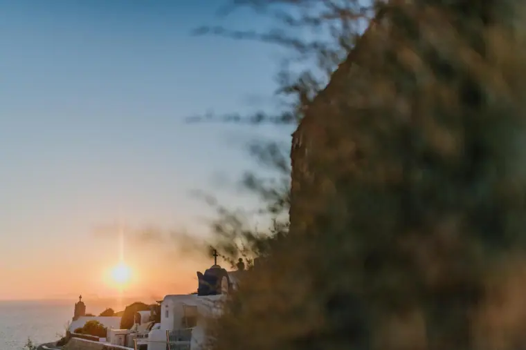 Sun setting over the sea behind silhouetted white houses in Santorini