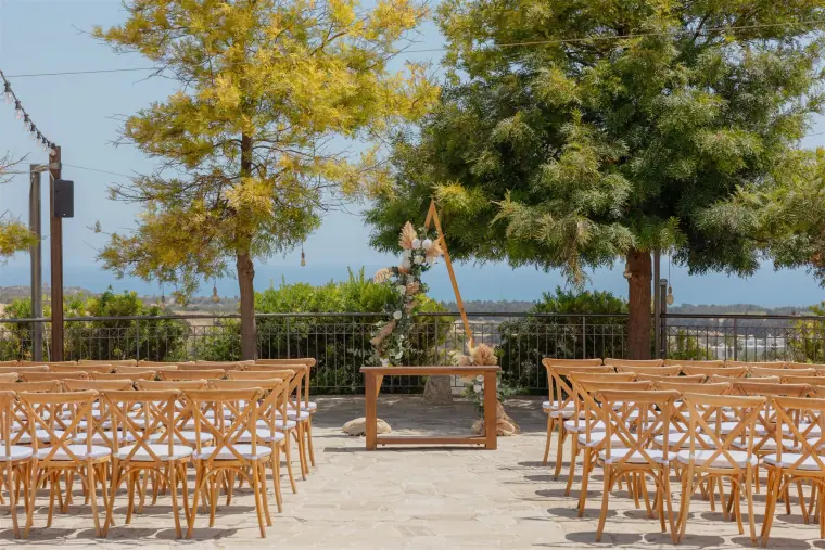 Wooden cross-back chairs set for an outdoor ceremony under the trees at Liopetro