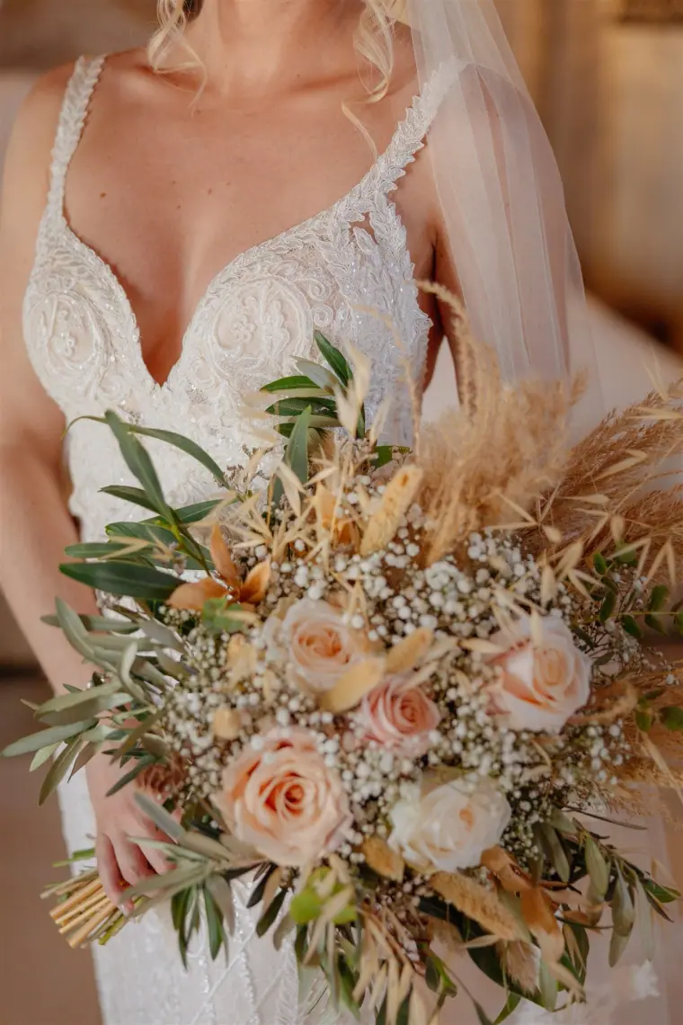 Close-up of the bride holding a boho bouquet of peach roses and pampas