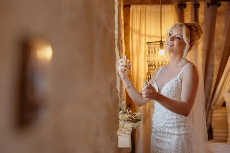 Bride spritzing perfume in a warm stone-walled room
