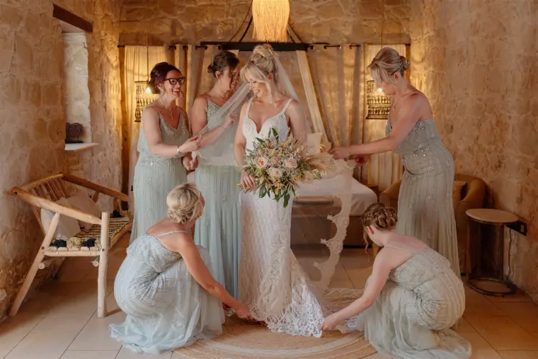 Bridesmaids in sage green helping Sarah with her dress