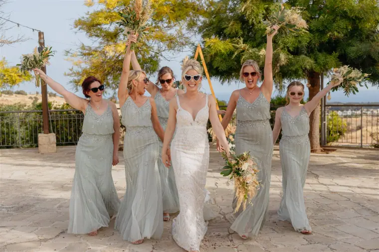 Bride and bridesmaids in sage green cheering with their bouquets raised