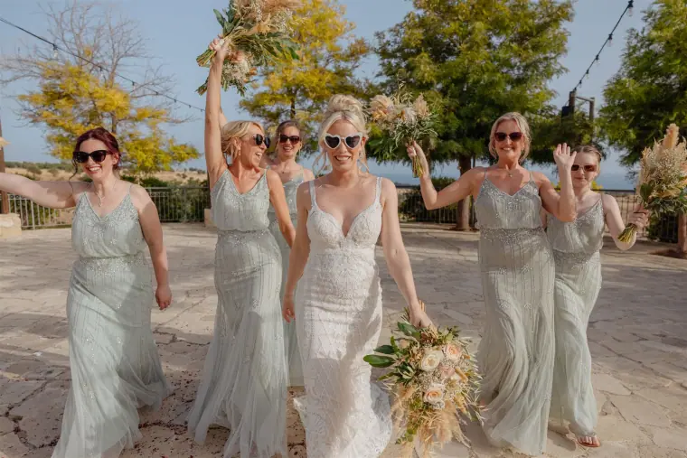 Bride walking with laughing bridesmaids, bouquets held aloft
