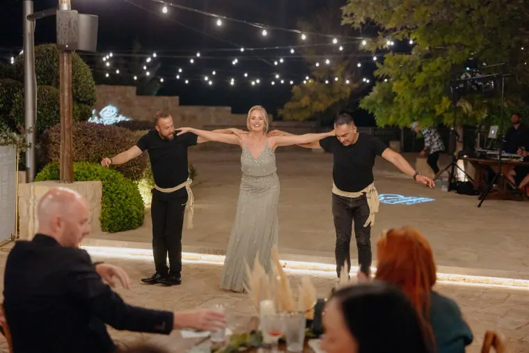 Bridesmaid joining two dancers in a traditional Greek dance at night