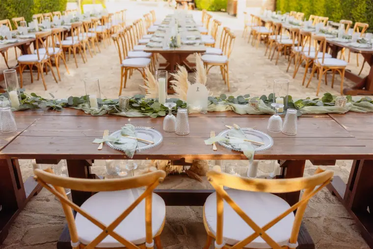 Long wooden reception tables with cross-back chairs and greenery runners