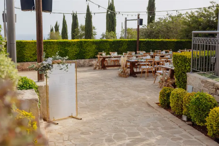 Courtyard with a white welcome sign and long tables lined by hedges at Liopetro
