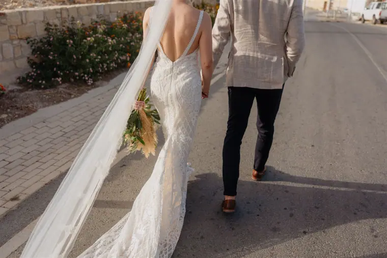 Bride's long veil trailing as she walks with the groom down a lane