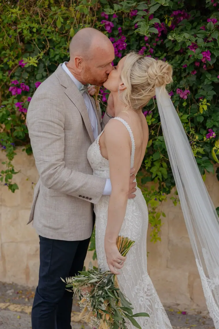 Ben kissing Sarah in front of pink bougainvillea