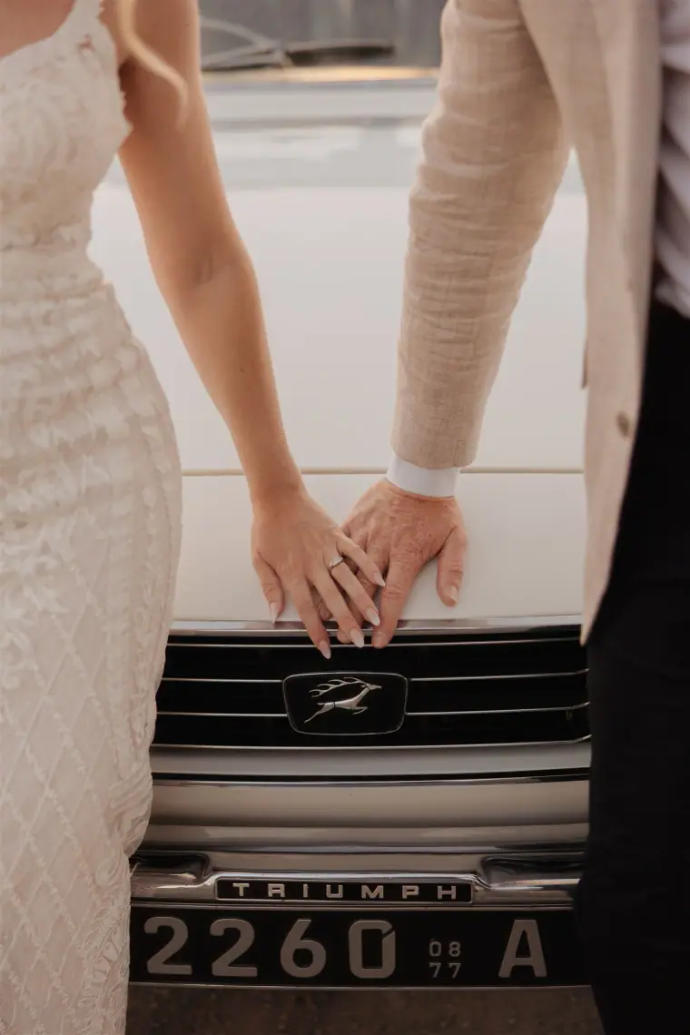 Couple's hands touching on the bonnet of the white Triumph