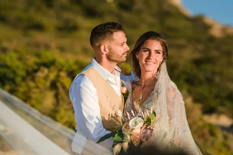 Kenton and Hassiba smiling together on a green hillside, bouquet in hand