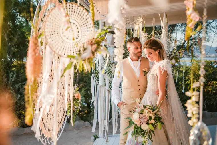 Bride and groom smiling beneath a pink-and-white macramé dreamcatcher