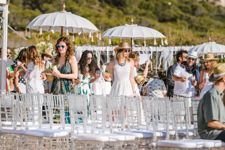 Guests in summer outfits arriving among white chairs and parasols