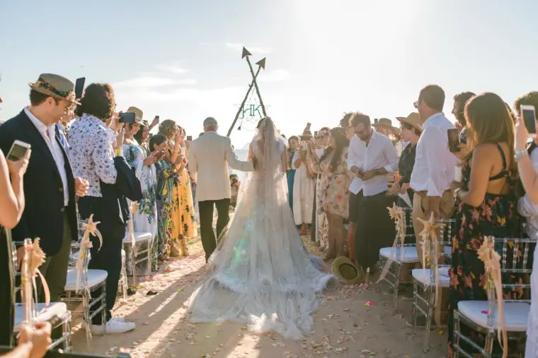 Bride walking down the aisle between standing guests towards the tipi arch