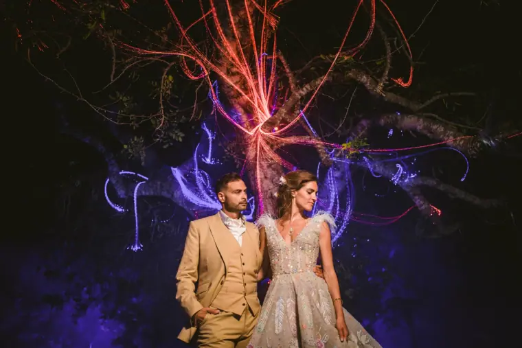 Couple standing beneath a tree lit with red and blue light patterns