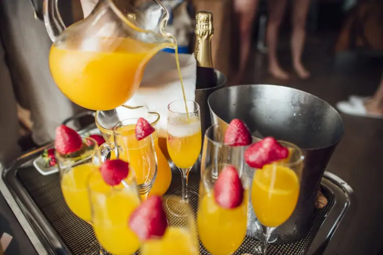 Tray of mimosas with strawberries beside a champagne bucket