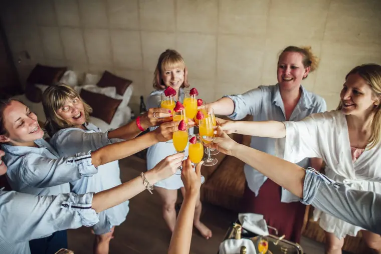 Bride and bridesmaids in matching shirts toasting with mimosas