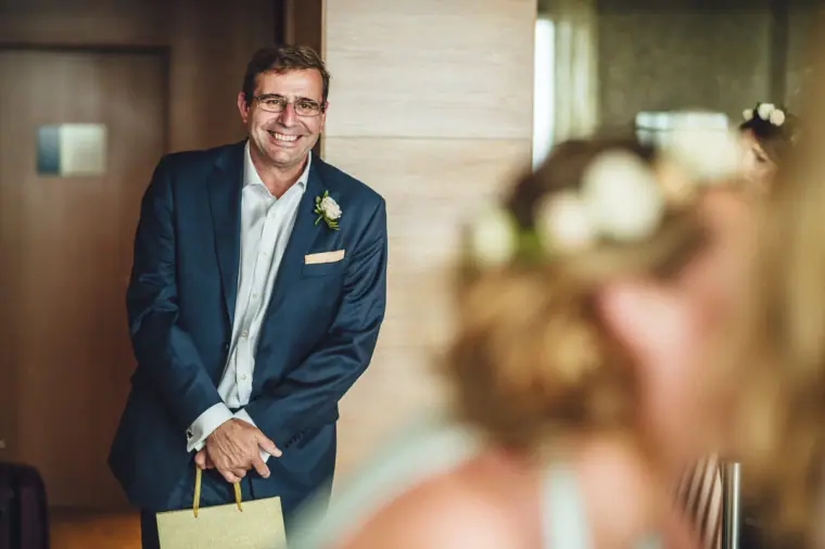 Man in a blue suit smiling with a gift bag while the women get ready