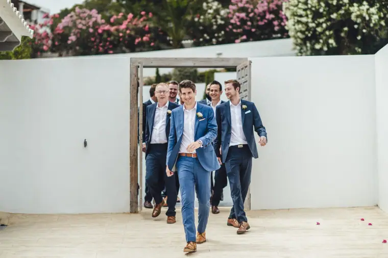 Groom and groomsmen in blue suits walking through a white gateway
