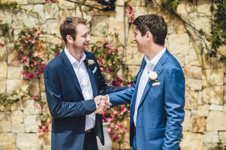 Groom shaking hands with a groomsman in front of bougainvillea