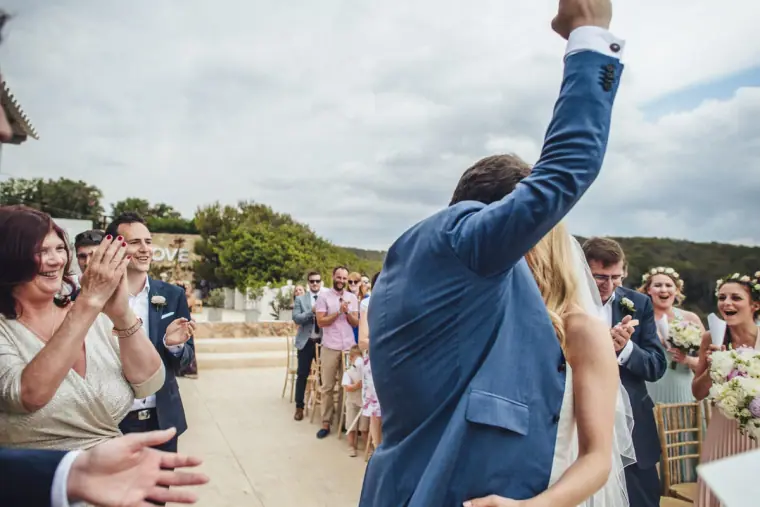 Groom punching the air as guests cheer after the ceremony