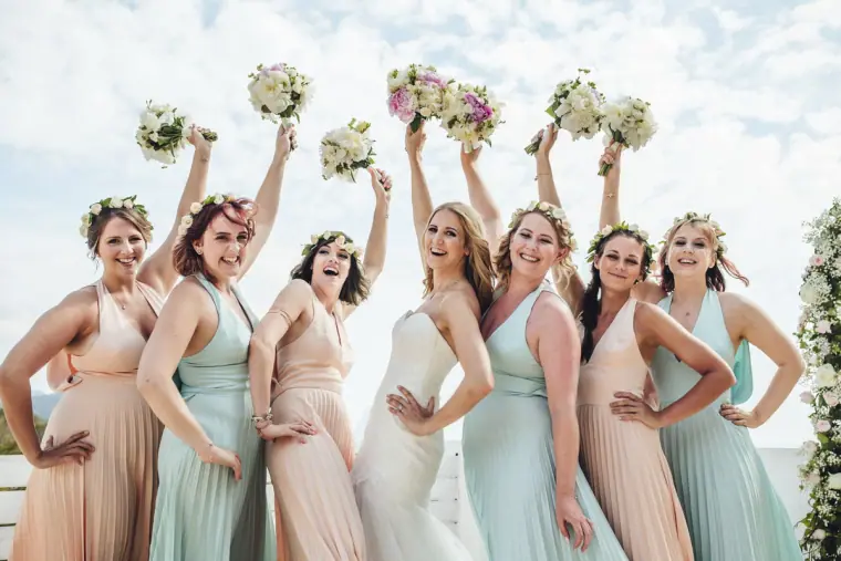 Bride and bridesmaids in pastel gowns throwing their bouquets in the air