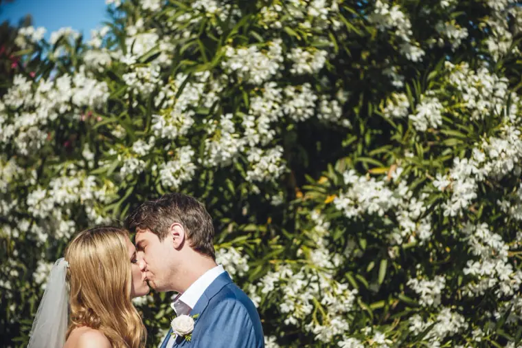 Stephanie and Paul kissing in front of a white-flowering oleander