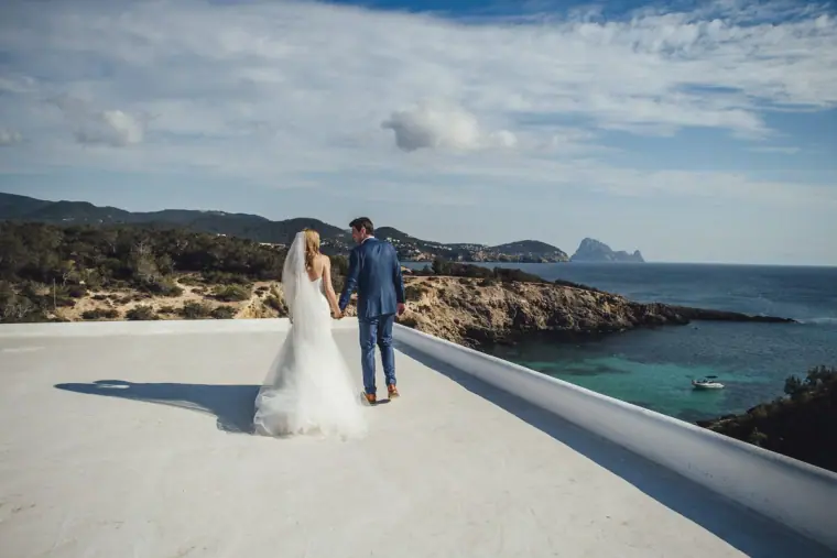 Couple standing on a white rooftop above a rocky turquoise coastline