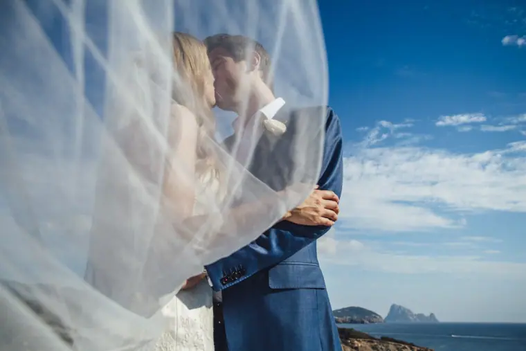 Couple kissing behind a windswept veil against a blue sky