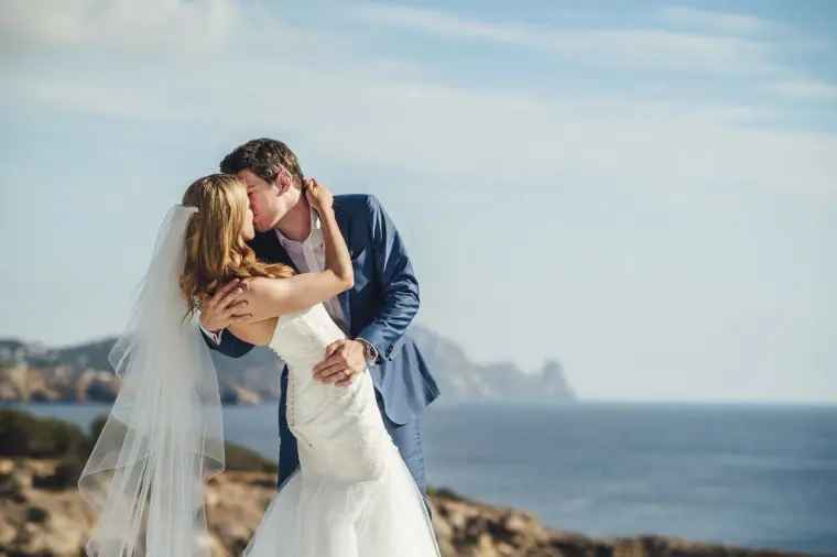 Groom dipping his bride for a kiss with the sea and islands behind