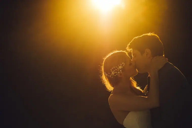 Bride and groom kissing in silhouette against a bright golden backlight