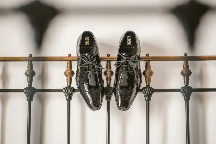 Groom's black patent shoes hanging on a wrought-iron bed frame