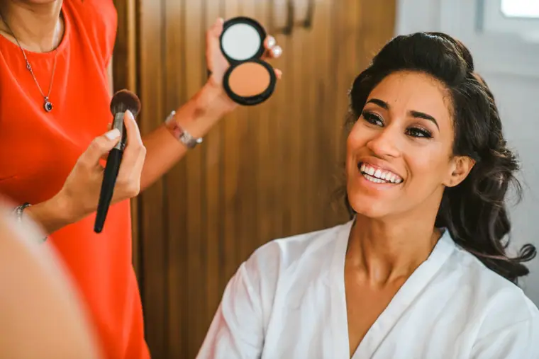 Bride smiling as a make-up artist holds up a powder compact and brush
